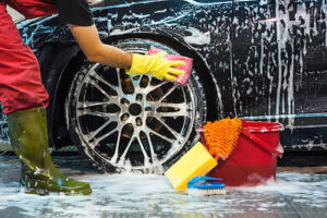 Man cleaning car tire with sponge.